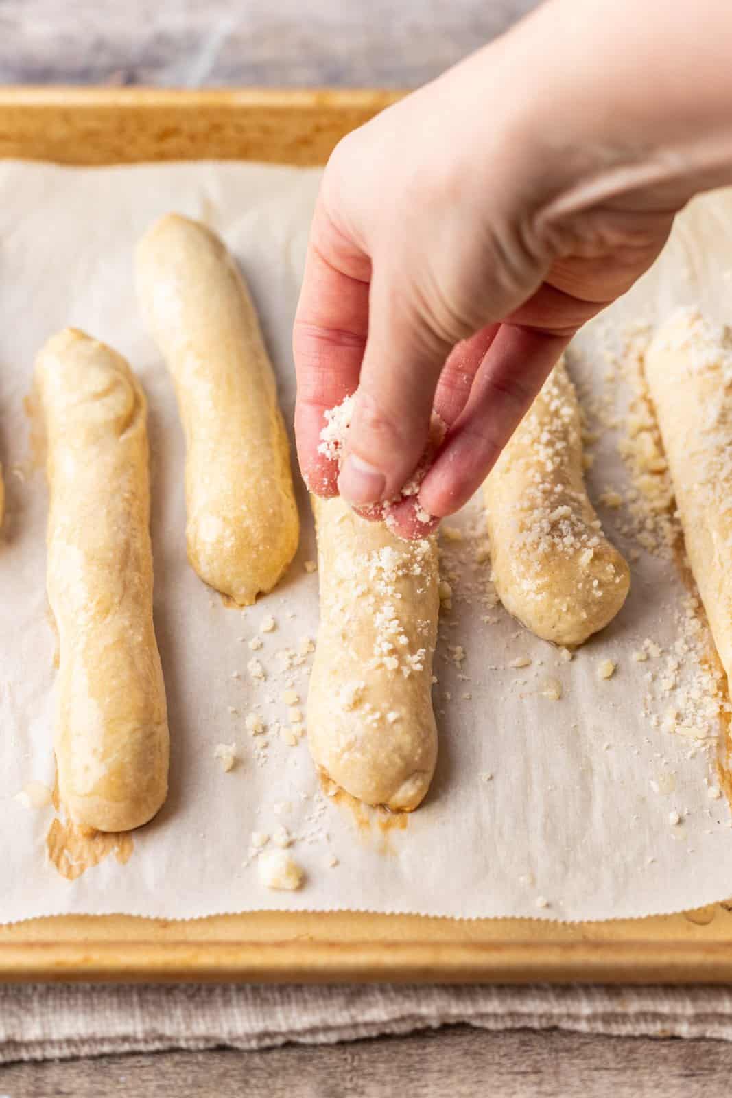 Breadsticks being sprinkled with parmesan cheese.