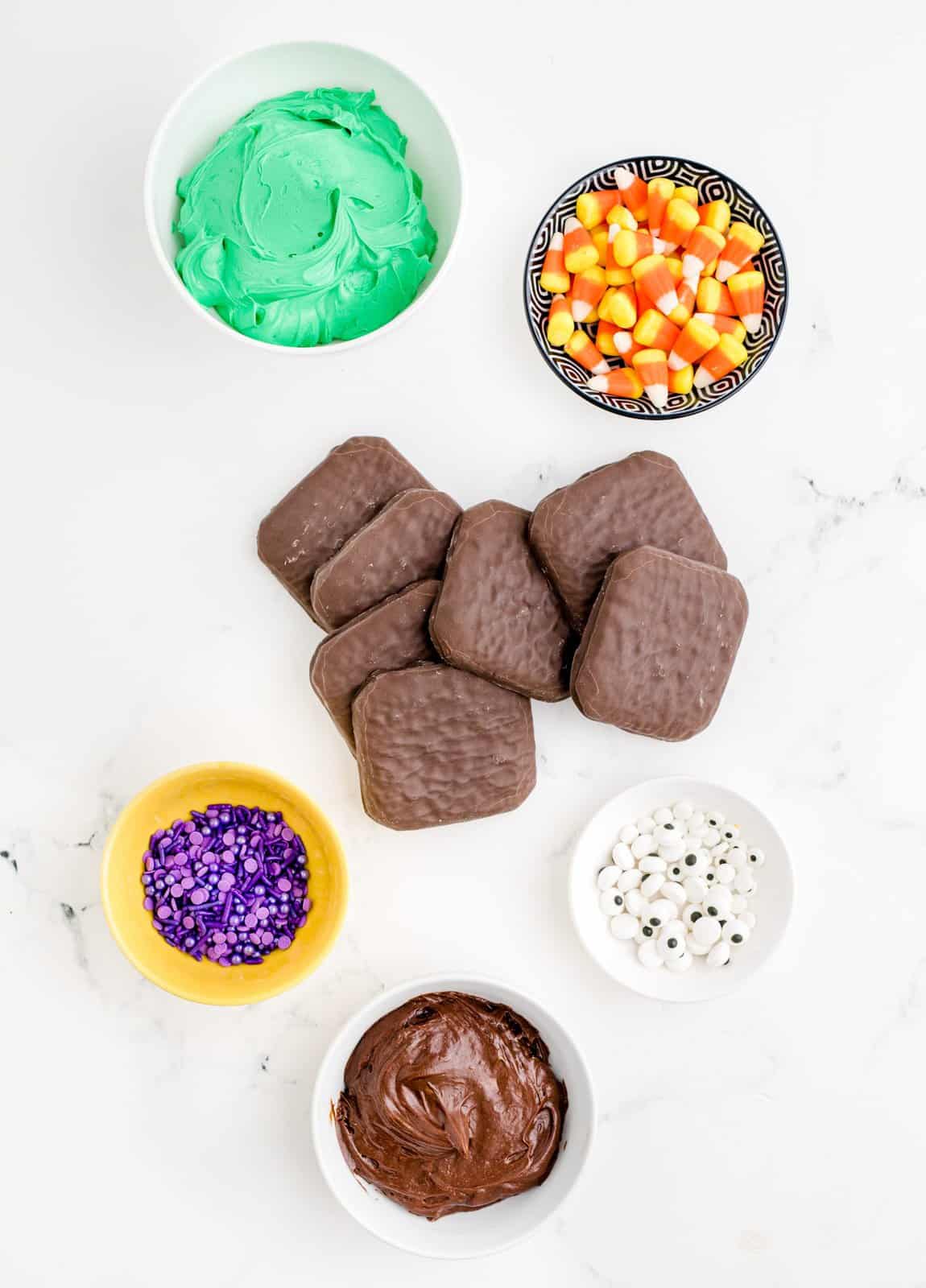 Ingredients needed: covered graham cracker cookies, green frosting, chocolate frosting, candy eyeballs (assortment of small and large), purple sprinkles and candy corn.