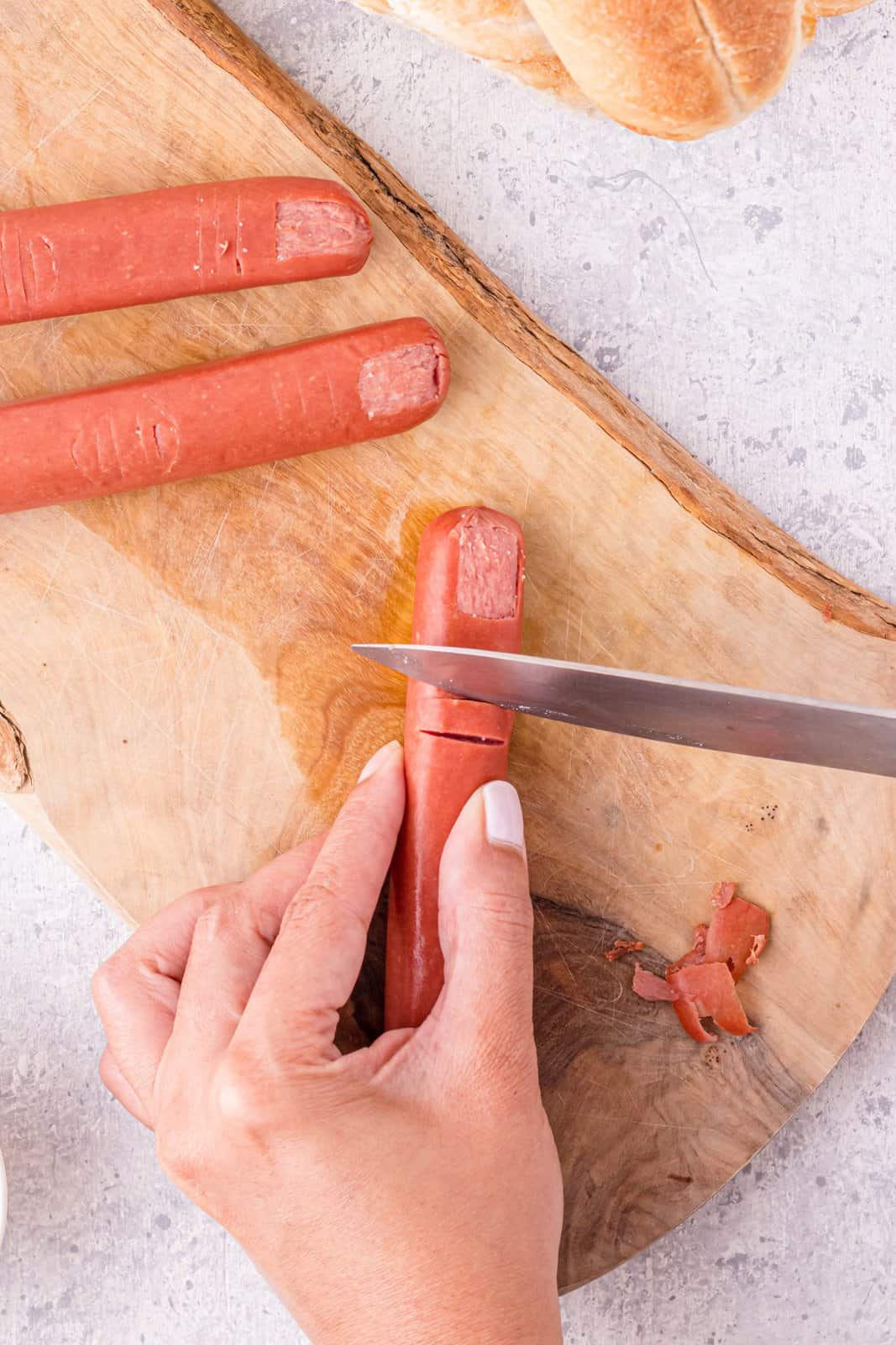 Knife cutting the upper knuckle creases in hot dog.