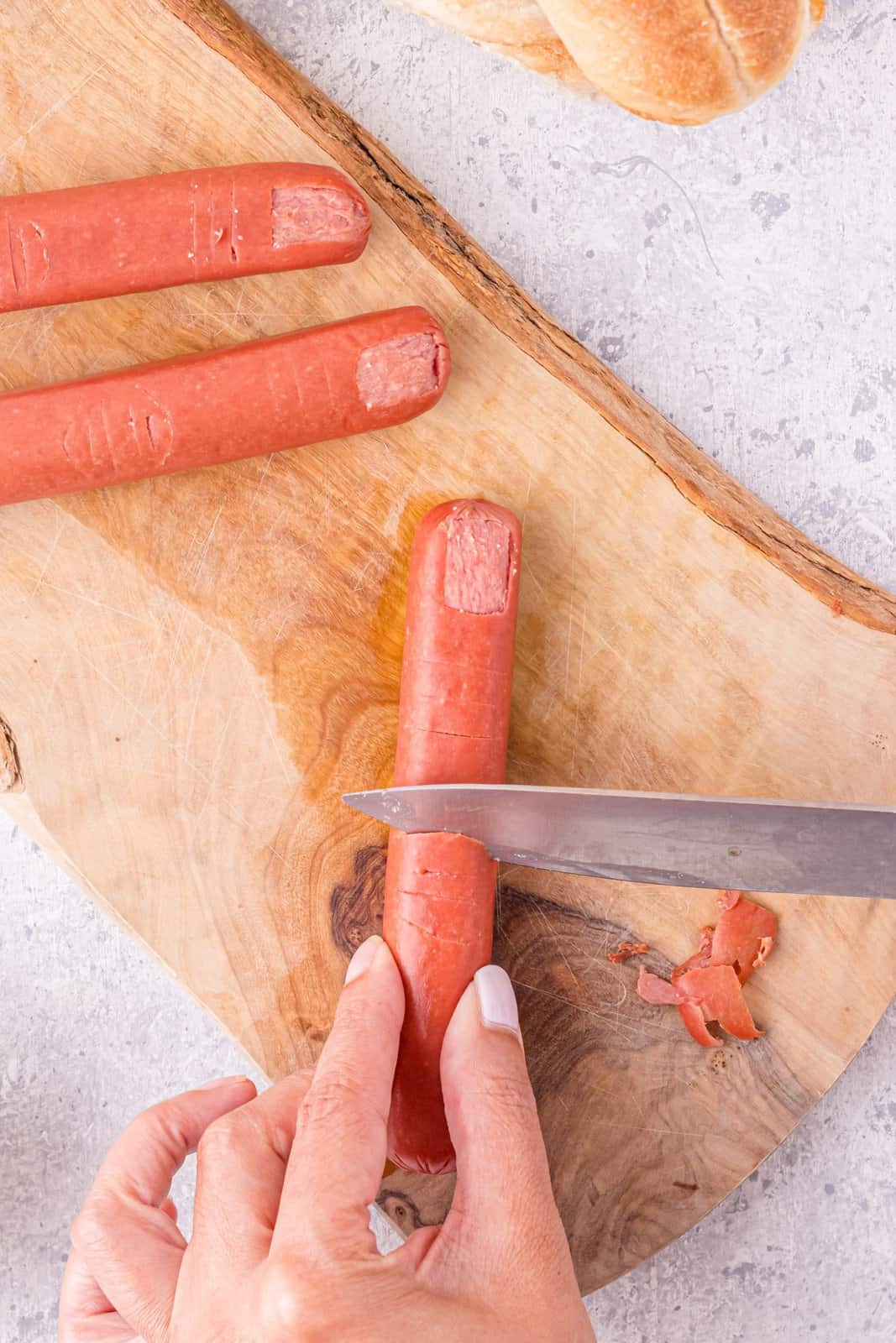 Knife cutting the lower knuckle creases in the hot dog.