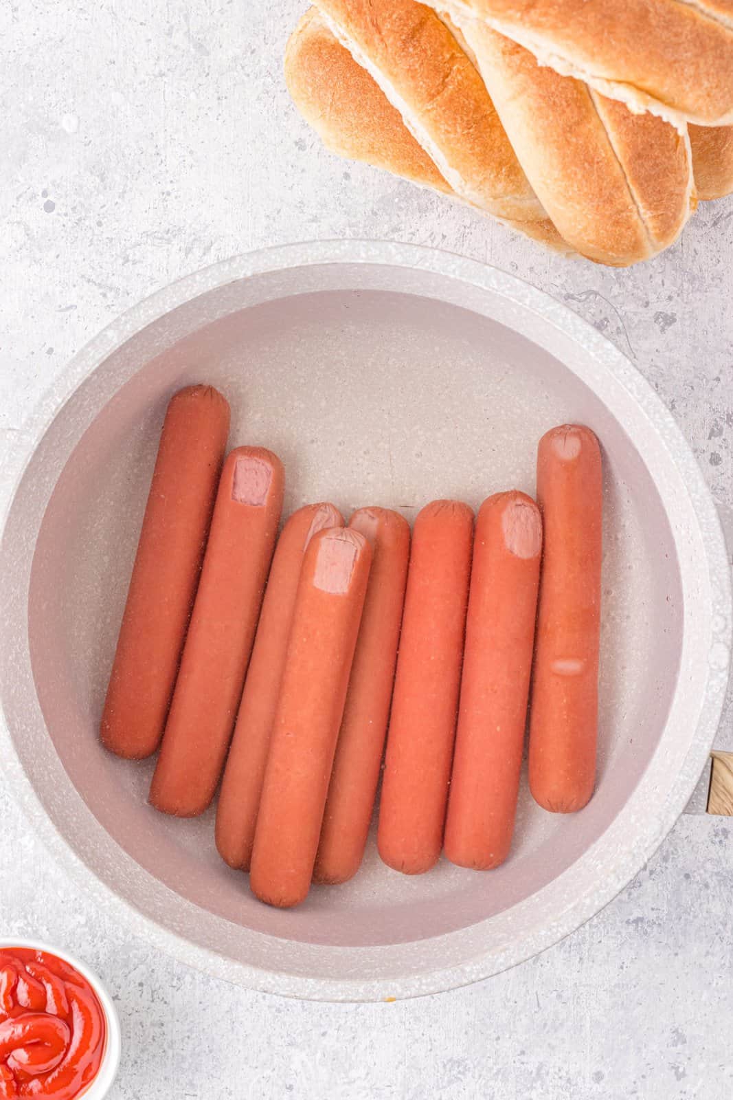 Hot dogs being boiled in pan.