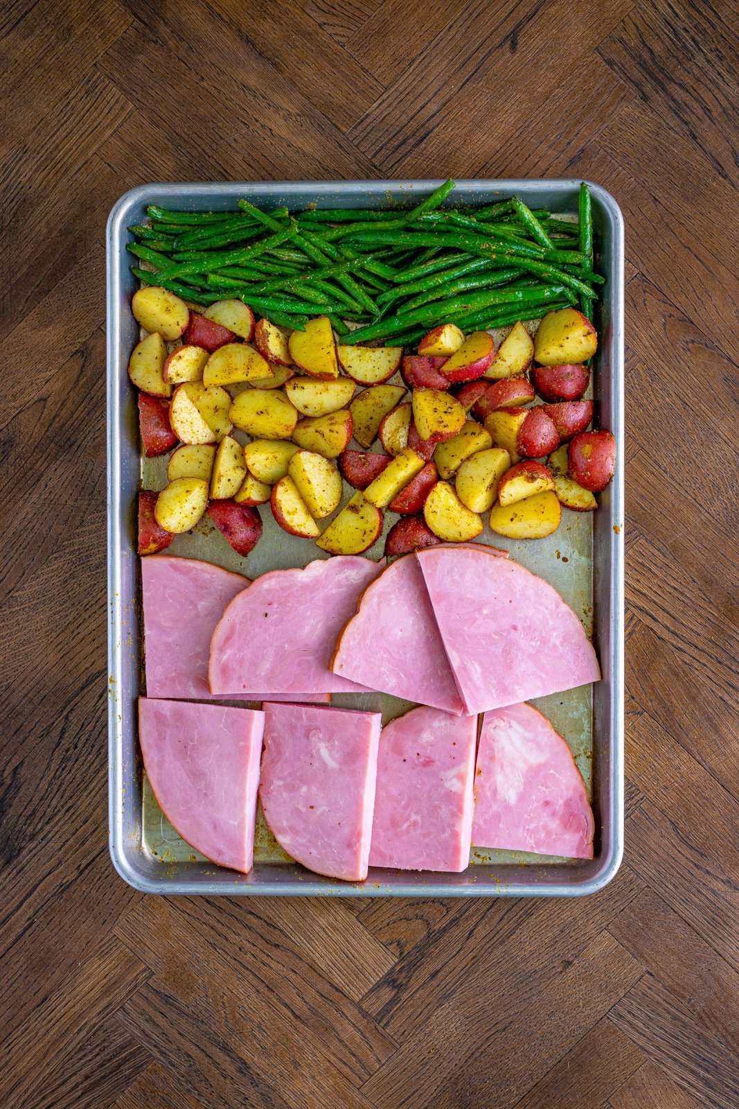 Potatoes and green beans pushed to one side of sheet pan and ham steaks added.