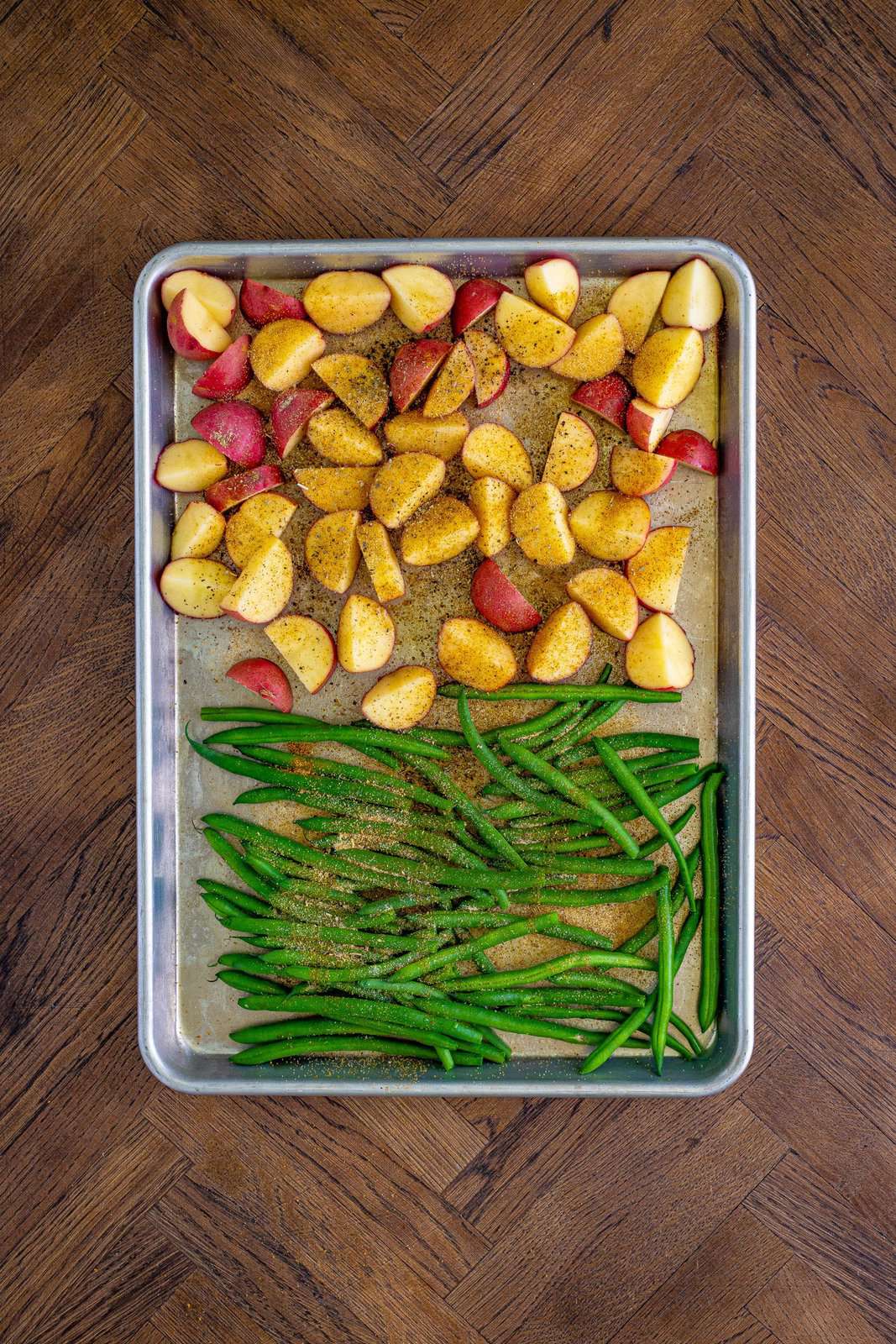Seasoning sprinkled over potatoes and green beans on sheet pan.