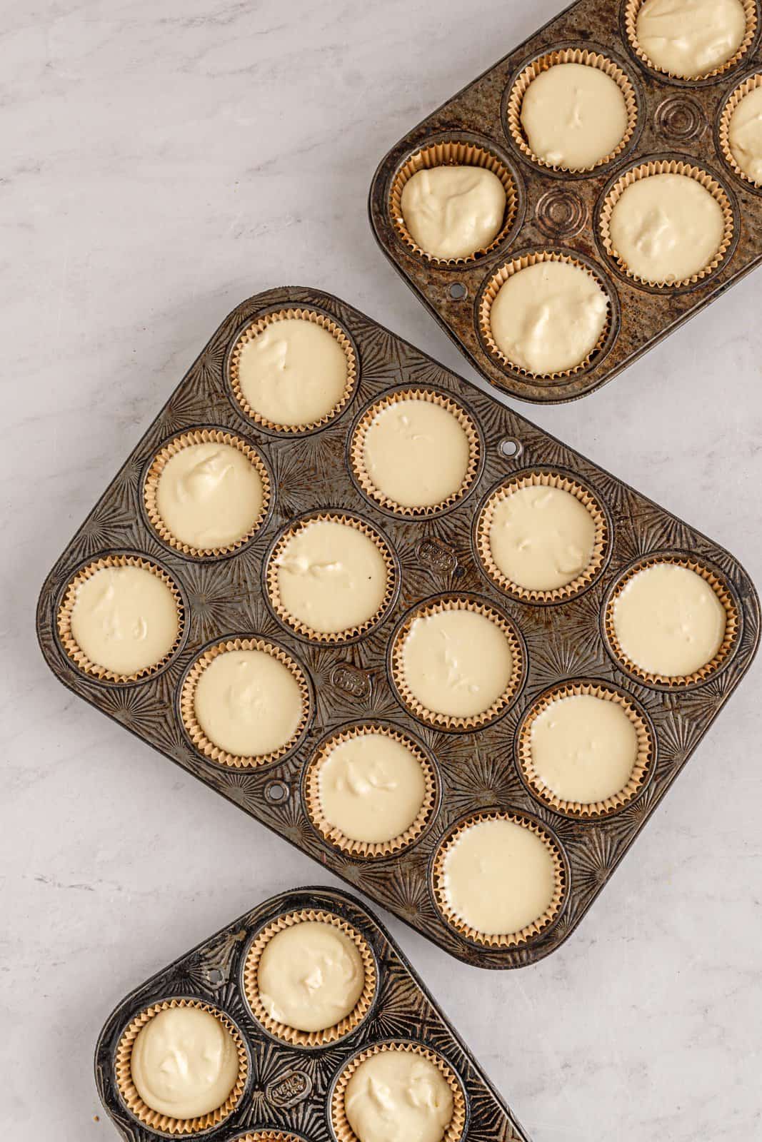 Cheesecake batter distributed among the wells of the muffin tins.