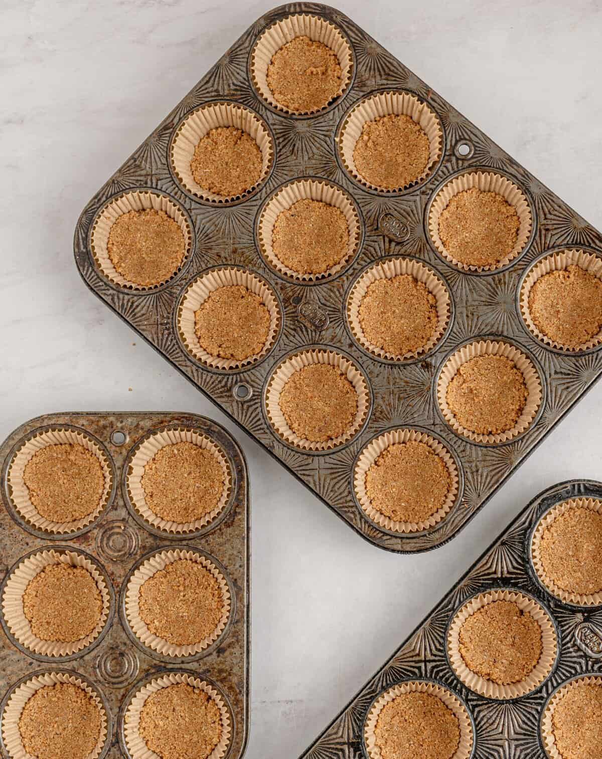 Muffin tins with paper liners with crust pressed into them.