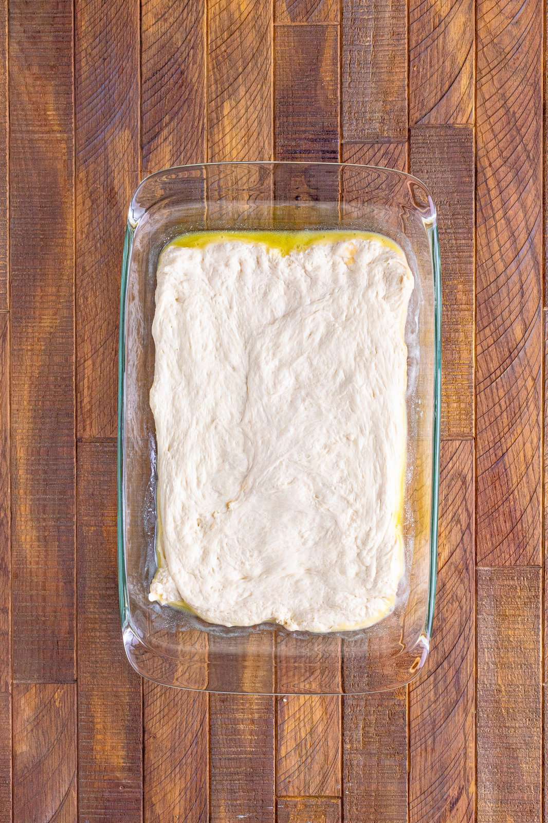 Pizza dough spread over butter in baking dish.
