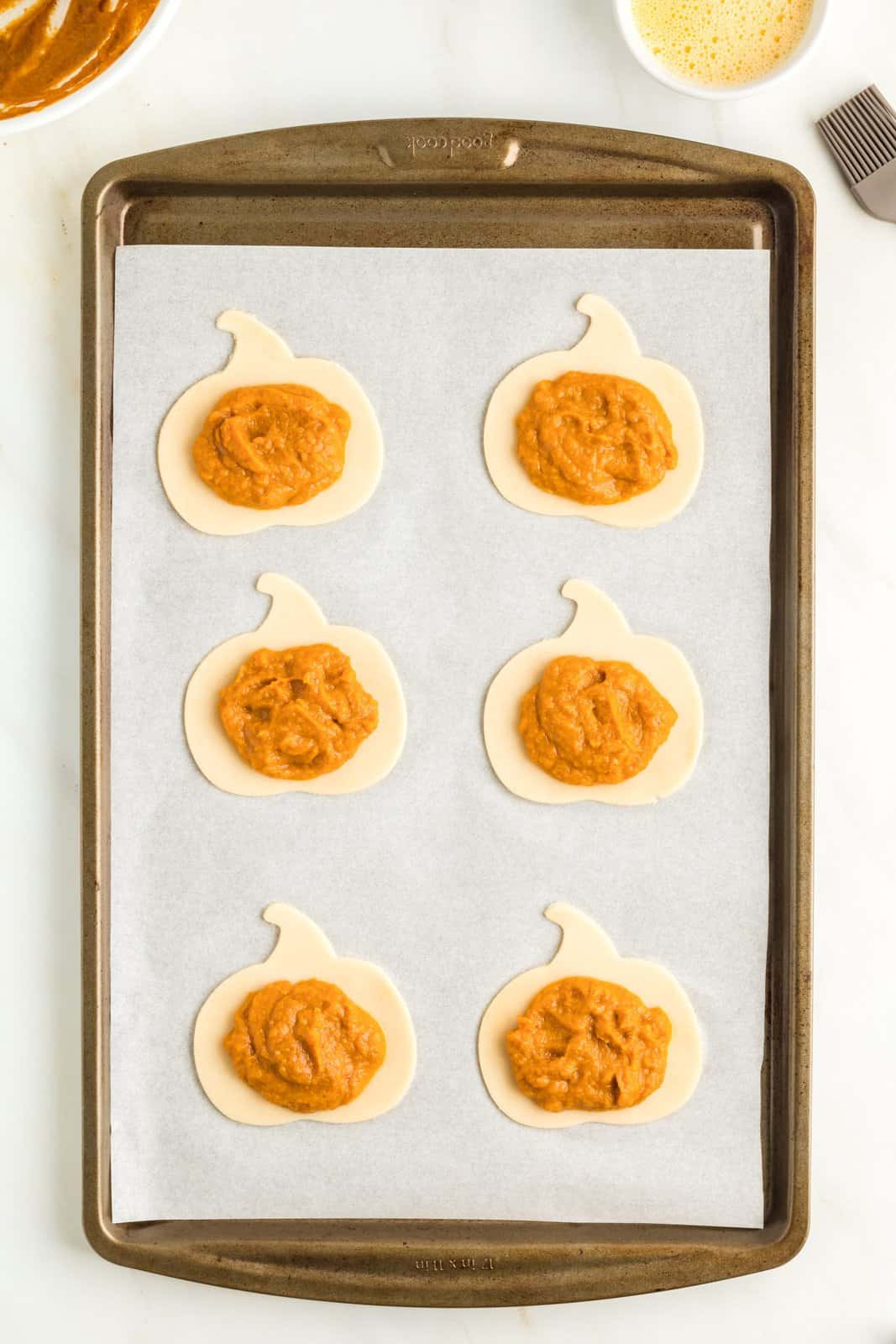 Cut pumpkin pie crust shapes on parchment lined paper with filling placed in center.