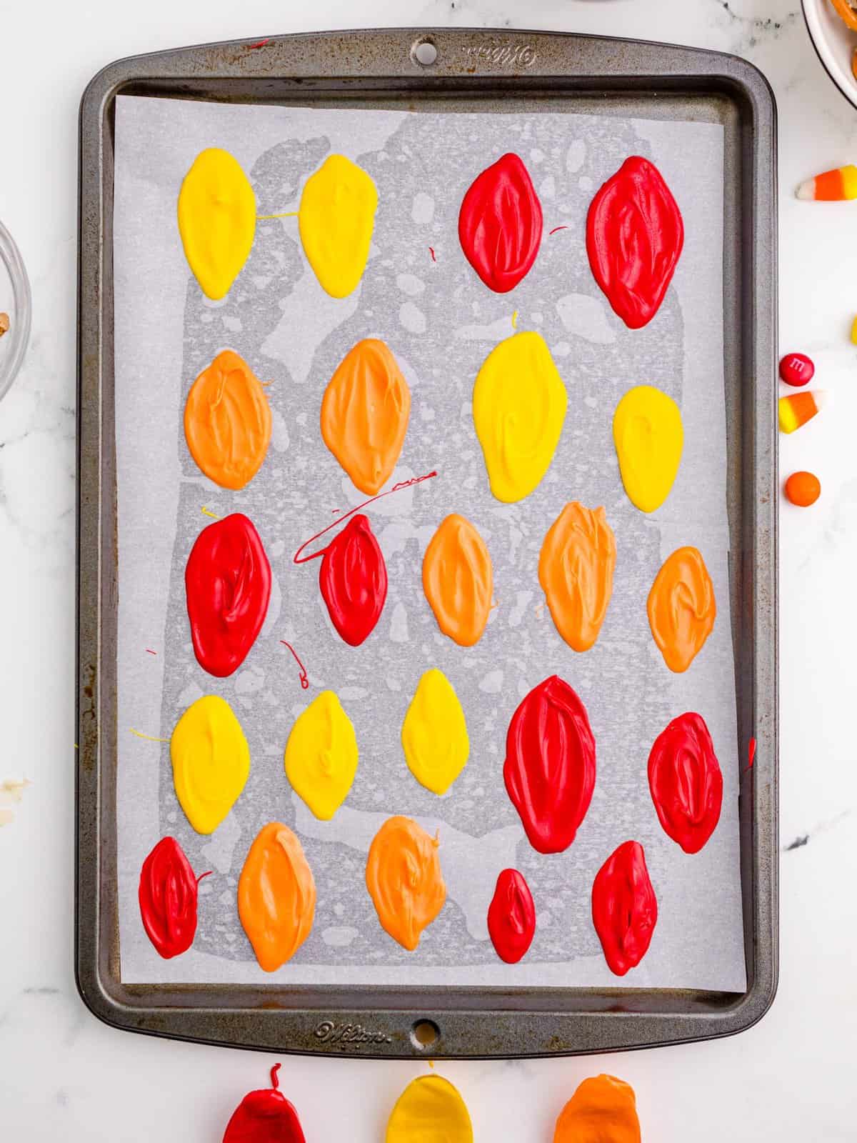 Candy melts spread into feather shapes on parchment lined baking sheet.