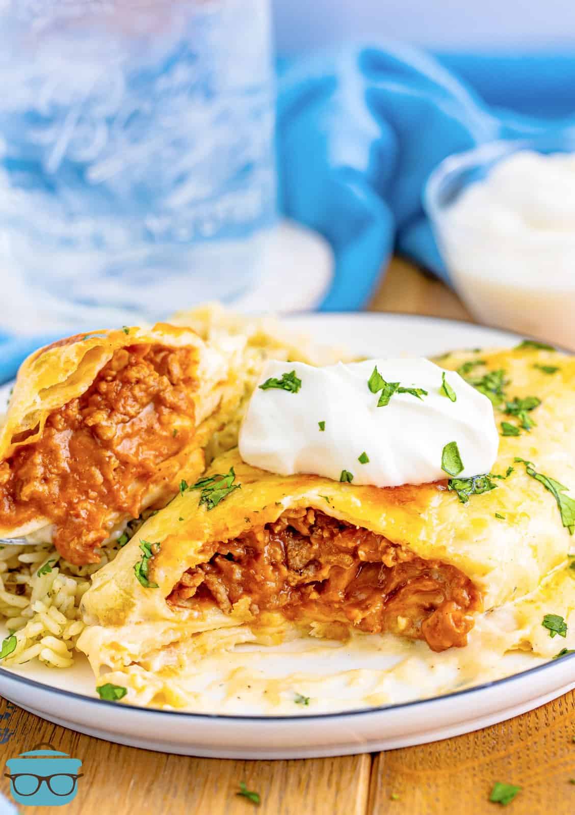 One of the Smothered Beef Burritos on white plate cut open showing the filling inside, topped with sour cream.