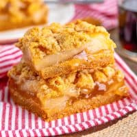 Close up square image of two Apple Crumble Bars stacked on top of one another on red and white linen.