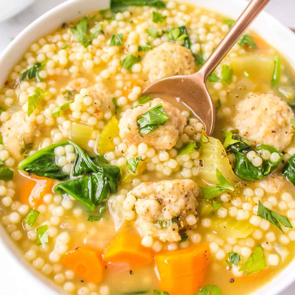Square close up of Italian Wedding Soup in bowl with gold spoon.