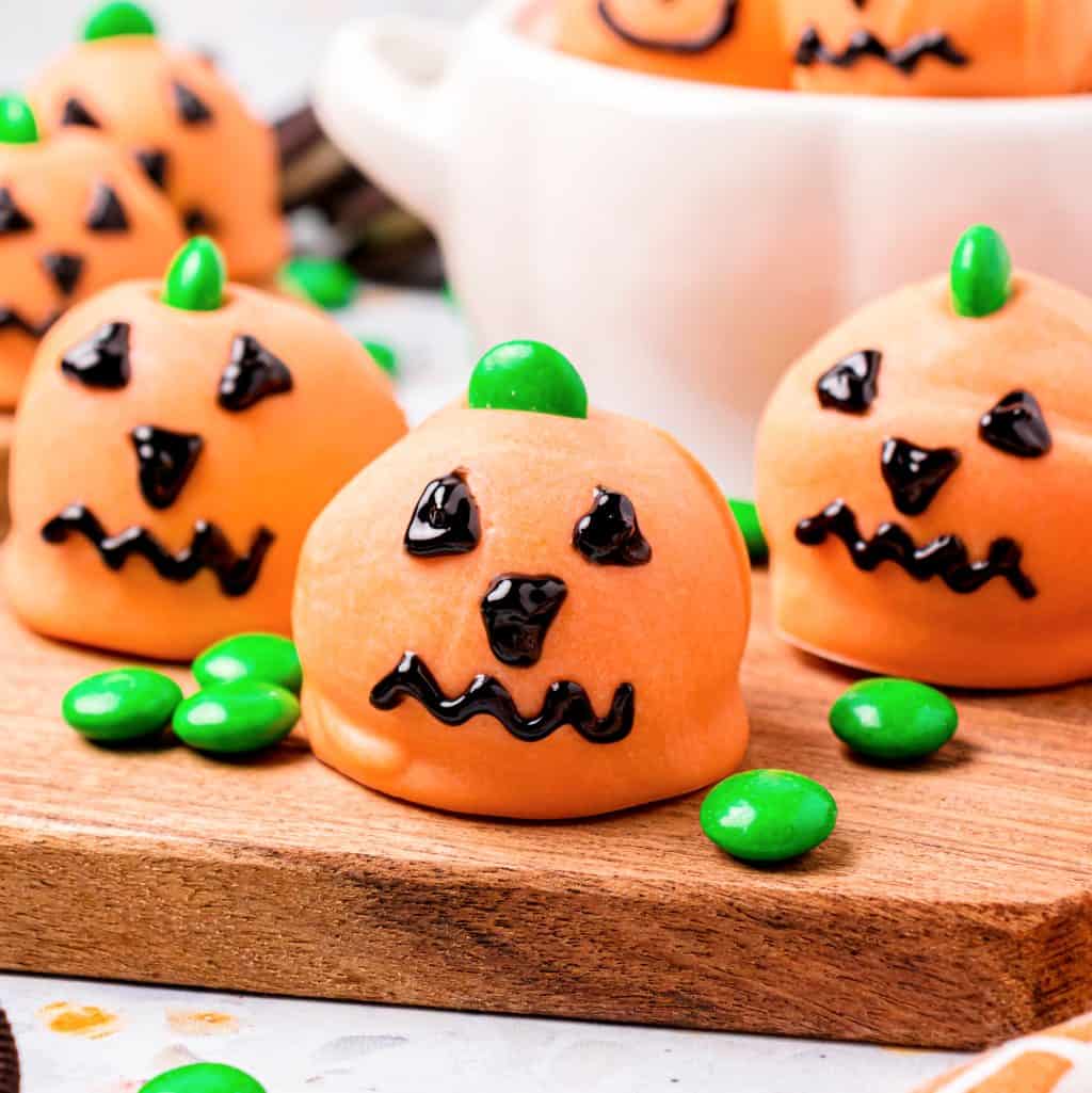 Close up square image of Jack-O-Lantern Oreo Balls on wooden board with green M&M's.