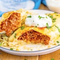 Close up of one of the Smothered Beef Burritos on white plate topped with sour cream cut open showing filling.