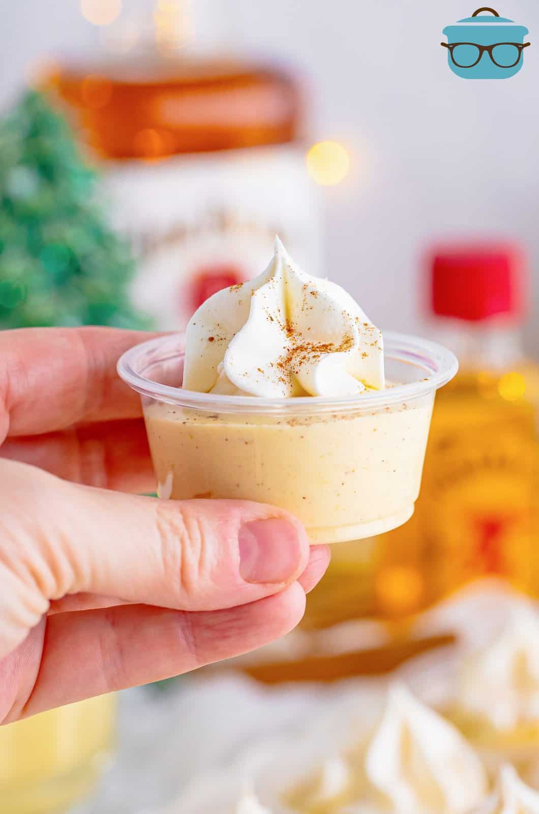 Hand holding up one of the Egg Nog Pudding Shots.