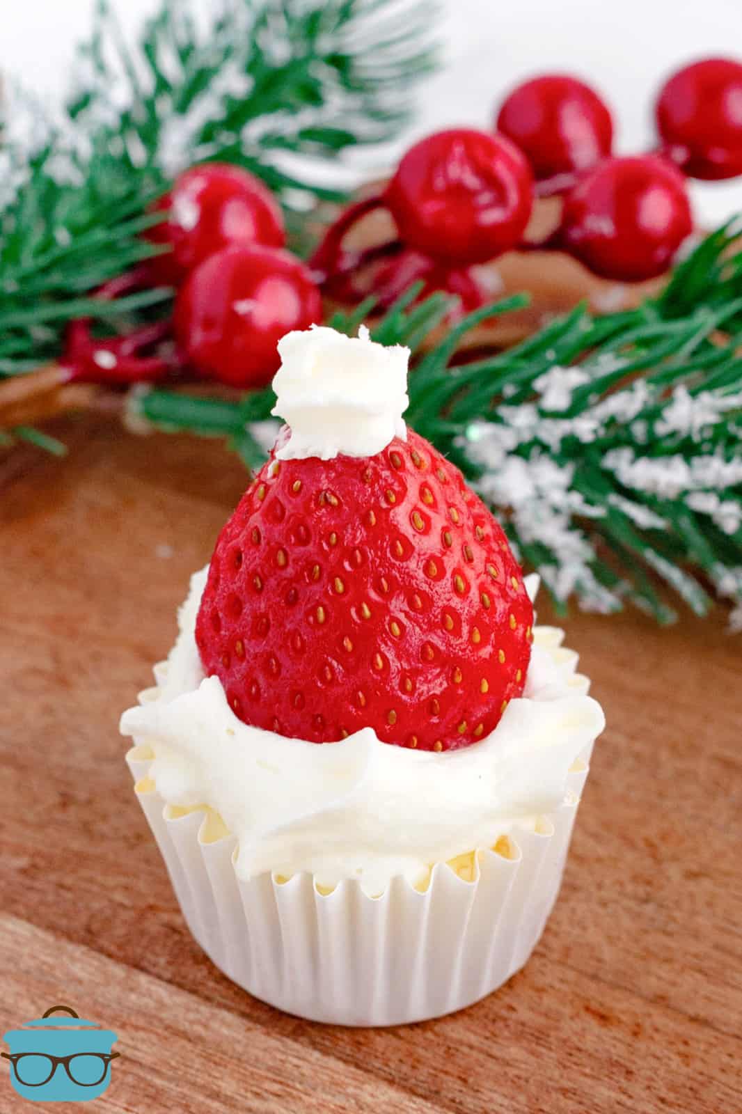 One of the Santa Hat Mini Cheesecakes on wooden board with decorations in background.