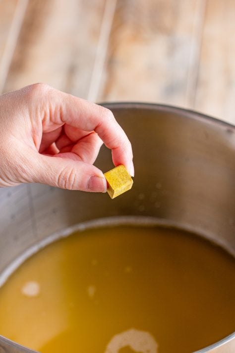 A bouillon cube being held over a pot.