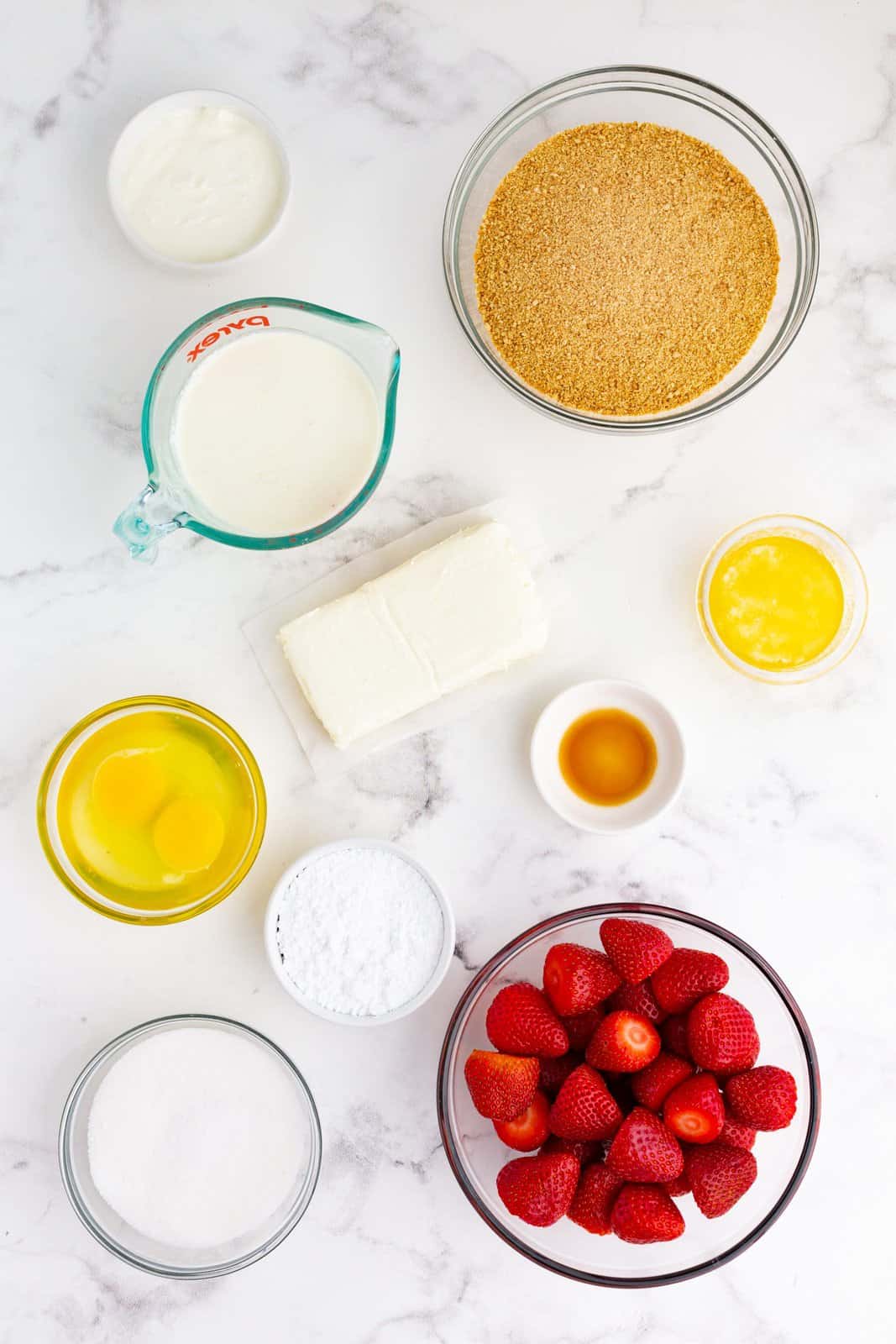 Ingredients needed: graham cracker crumbs, salted butter, cream cheese, granulated sugar, eggs, sour cream, vanilla extract, heavy whipping cream, powdered sugar and strawberries.