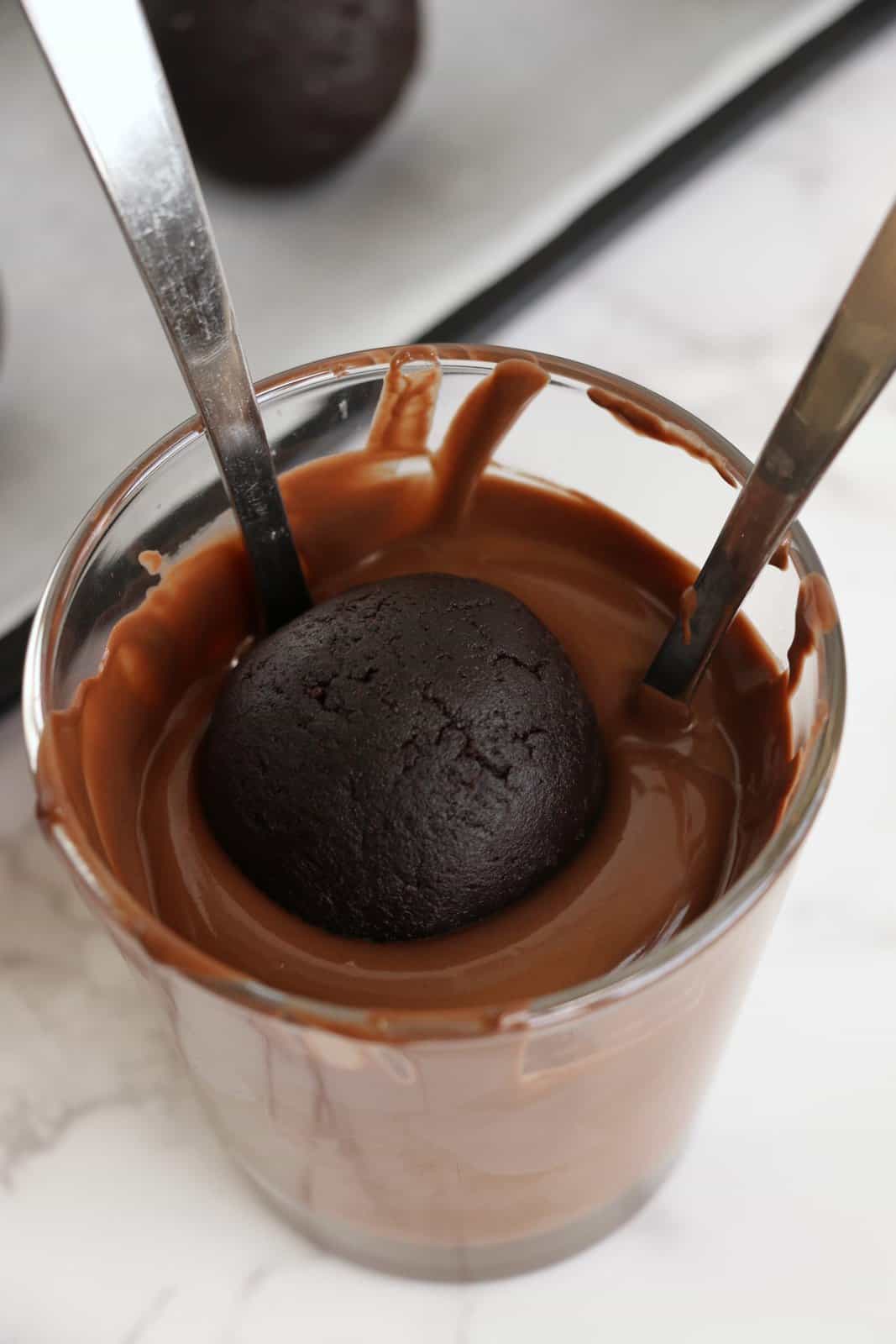 Melted chocolate in glass with cake ball being dipped into it.