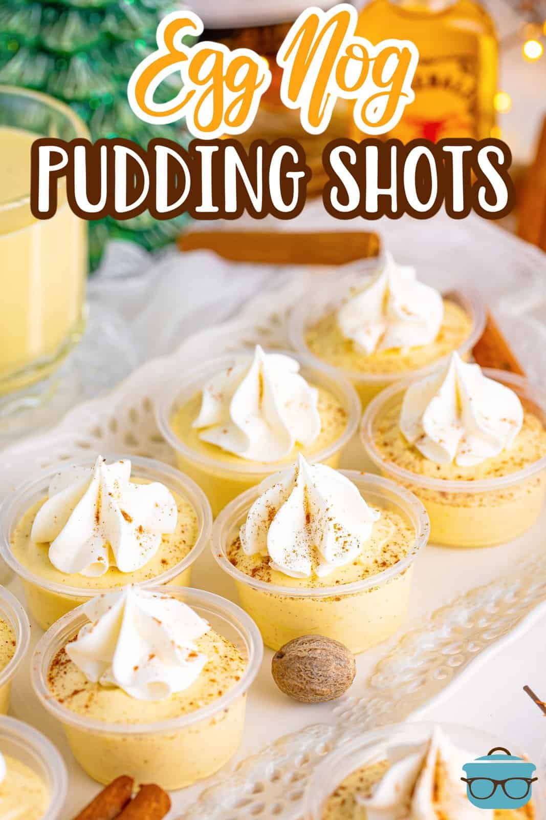 Slightly overhead Pinterest image of Egg Nog Pudding Shots on white platter, garnished with nutmeg and cinnamon sticks on platter.