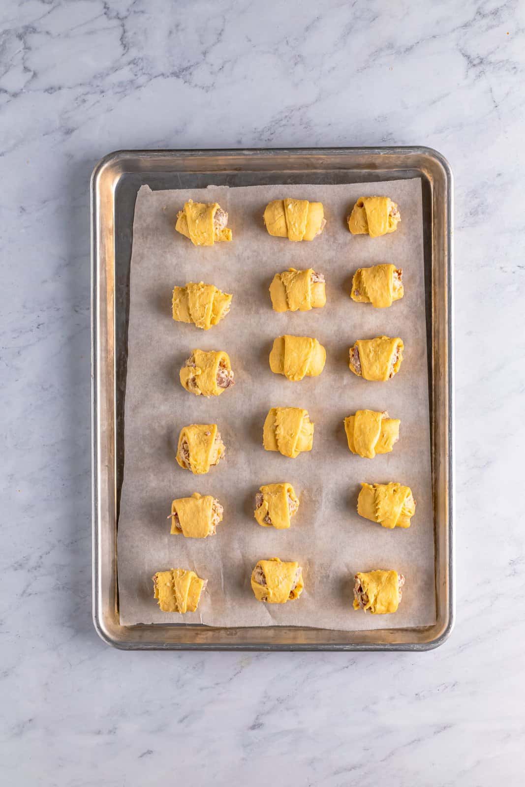 Rolled up crescent puffs on parchment lined baking sheet.