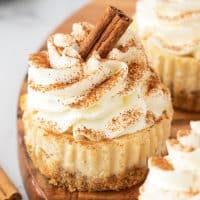 Close up square image of one of the Egg Nog Mini Cheesecakes topped with whipped cream, cinnamon and cinnamon stick.