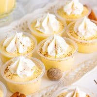 Close up of Egg Nog Pudding Shots on white platter with whipped topping and nutmeg and cinnamon on platter.