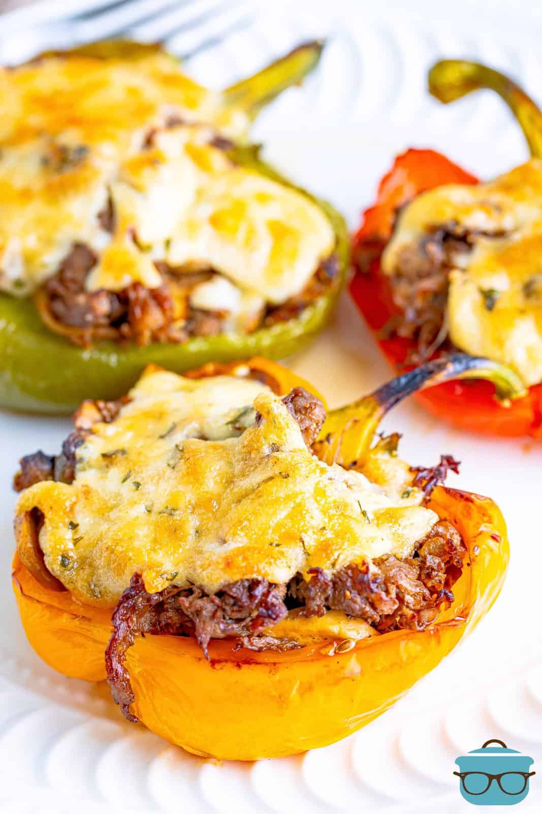 three cheesesteak stuffed peppers on a white round plate. 