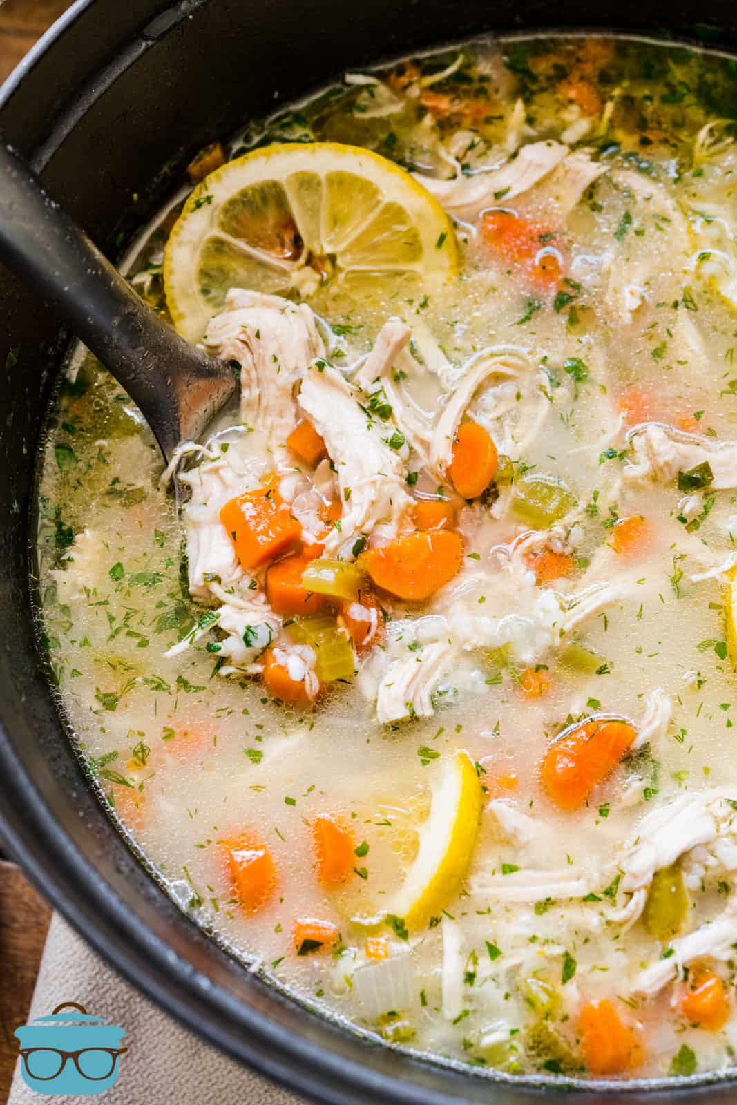 spoons inserted into a large pot with lemon chicken rice soup.