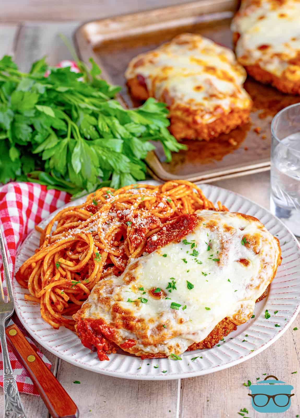 A white plate with a piece of homemade chicken parmesan and a side of spaghetti next to it.