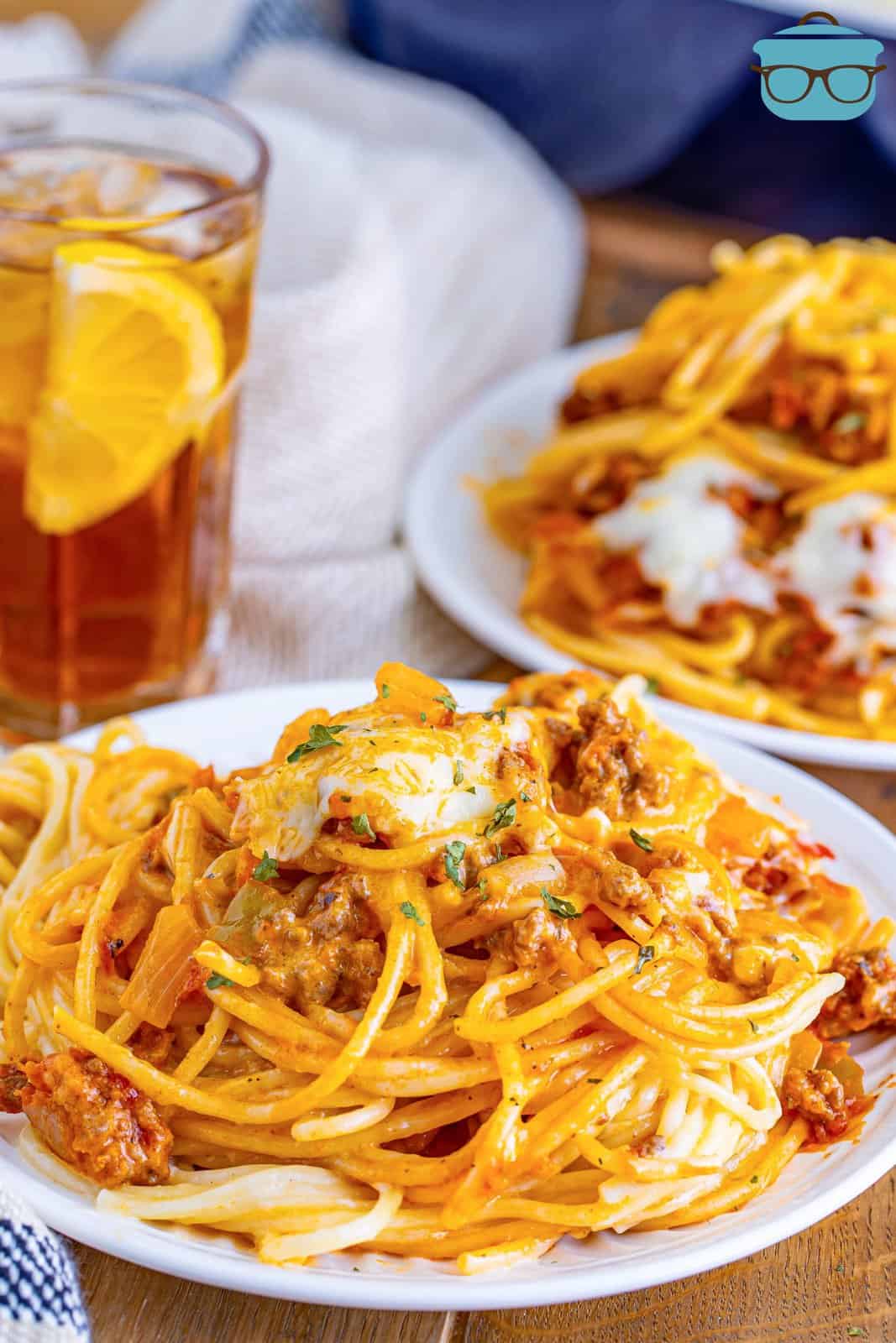 a round white plate with a serving of million dollar spaghetti on top with a glass of iced tea in the background. 
