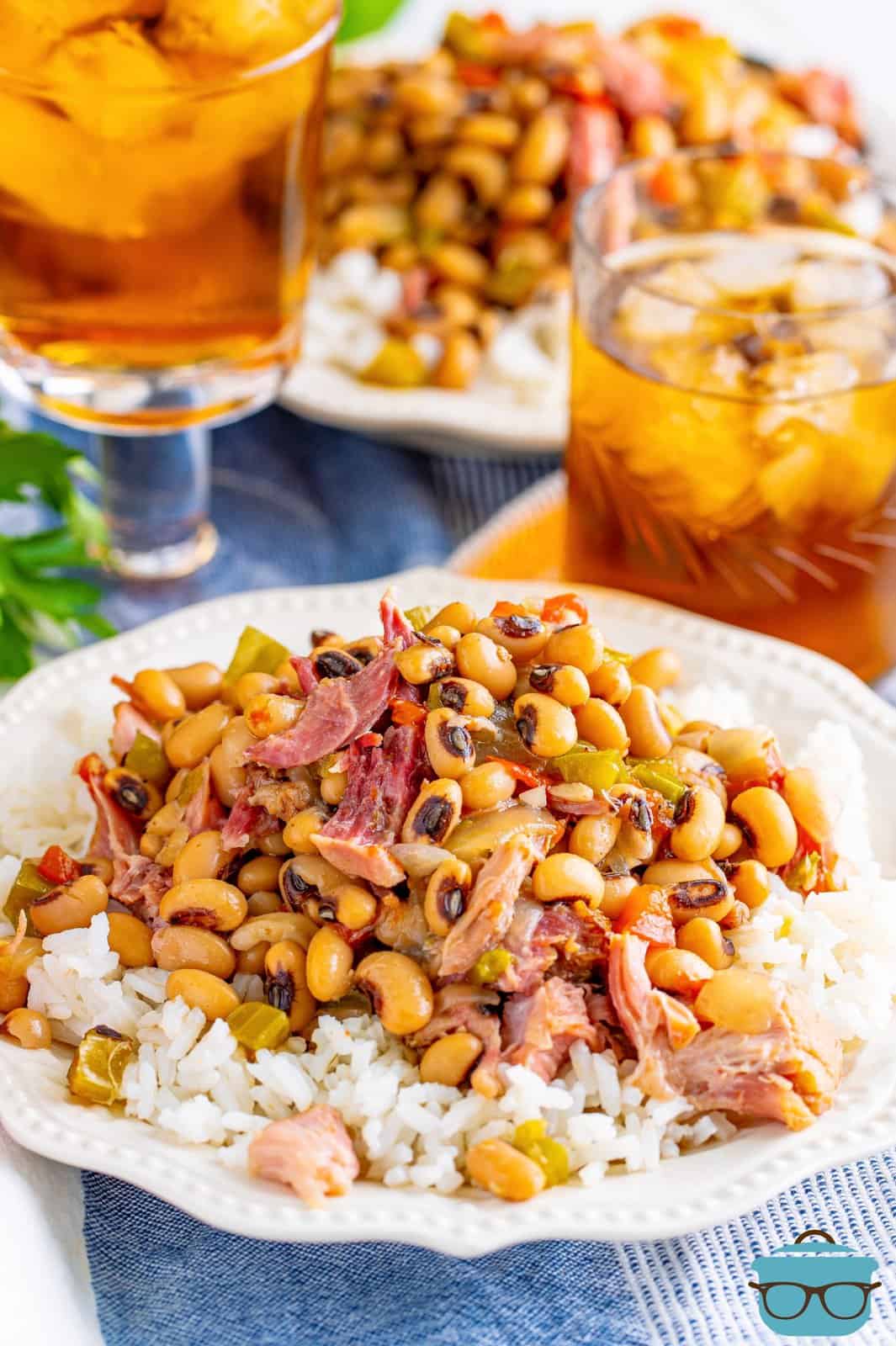 black eyed peas served over white rice on a white plate with a glass of iced tea in the background.
