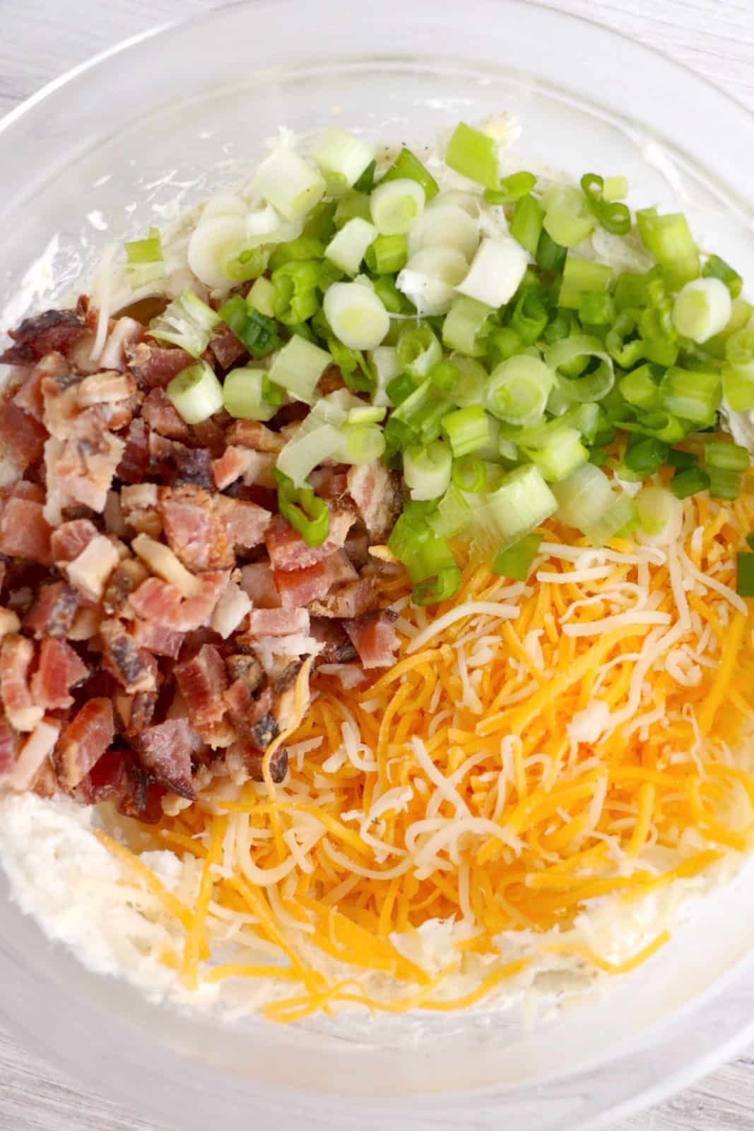 sliced cheese, chopped bacon and sliced onions added to cream cheese mixture in a bowl.