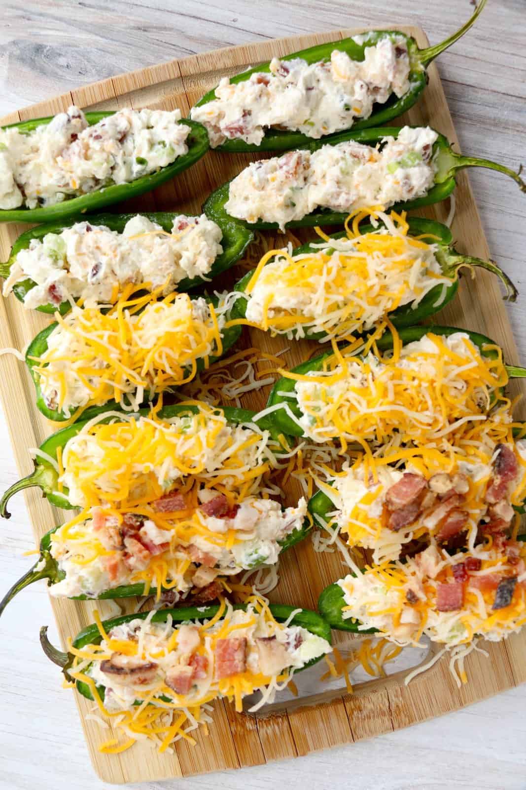 jalapenos being shown stuffed with cream cheese mixture and being topped with sliced cheese and cooked bacon.