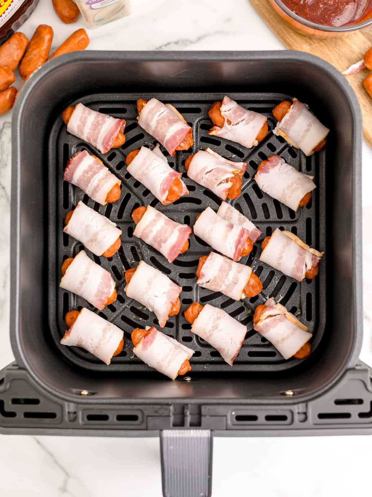 bacon wrapped sausages shown lined up in an air fryer basket. 