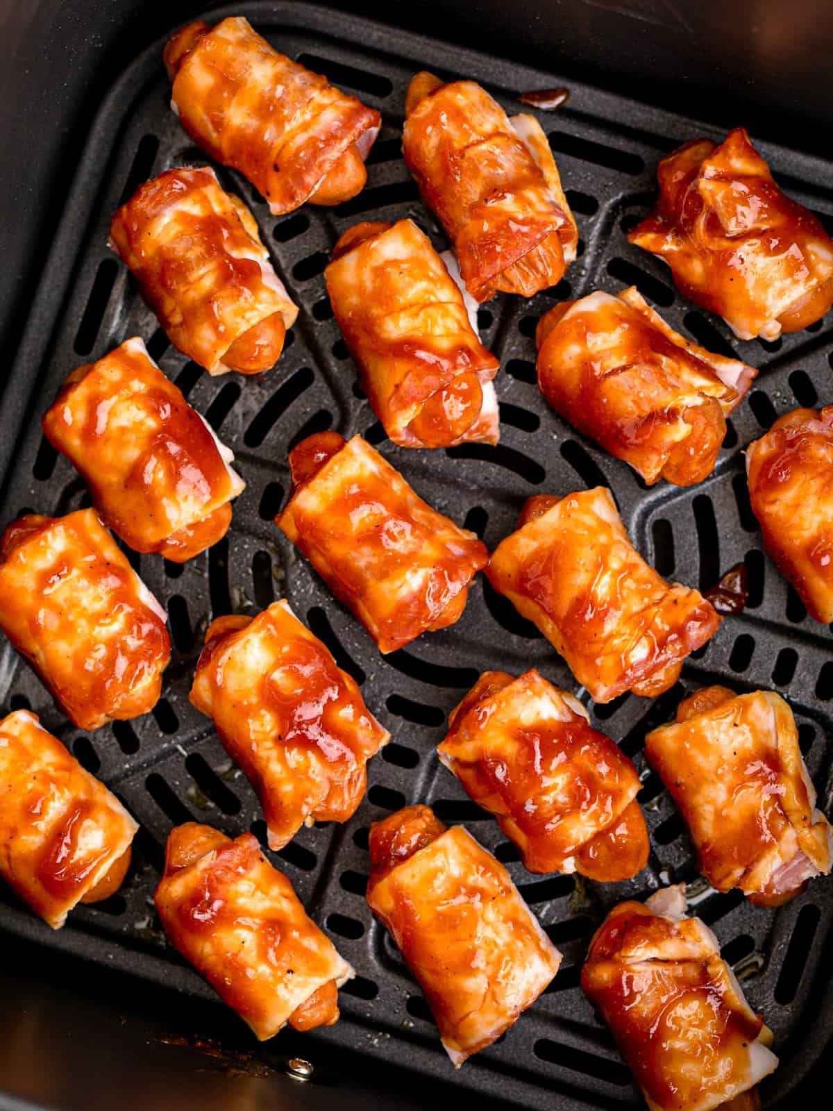 barbecue sauce coated bacon wrapped little smokies shown before cooking in the air fryer basket. 