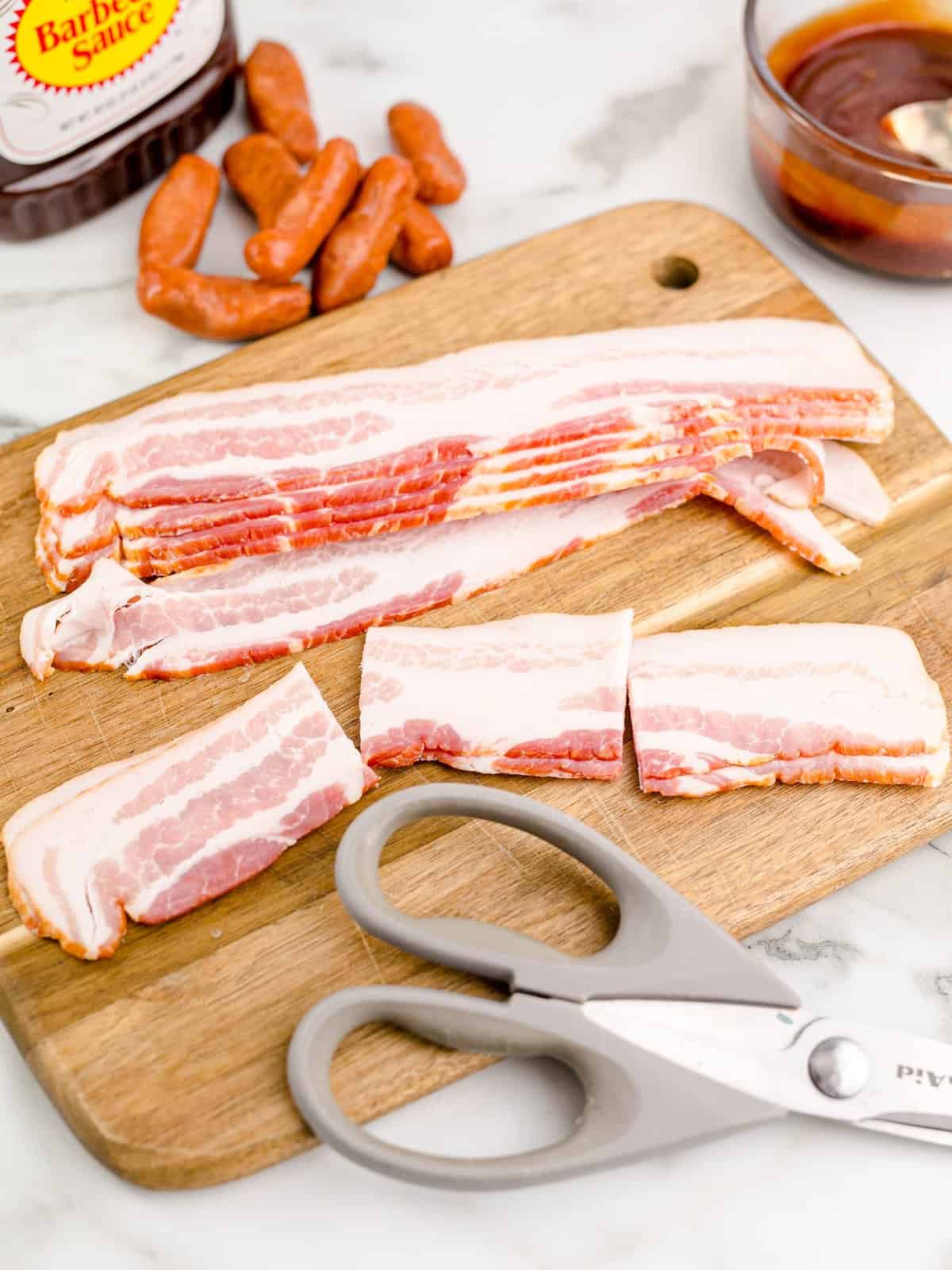 bacon shown cut into three pieces on a cutting board with kitchen scissors. 
