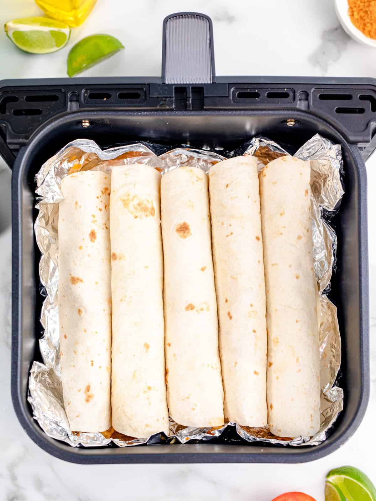 rolled up tortillas lined up and placed on the aluminum foil in the air fryer basket. 