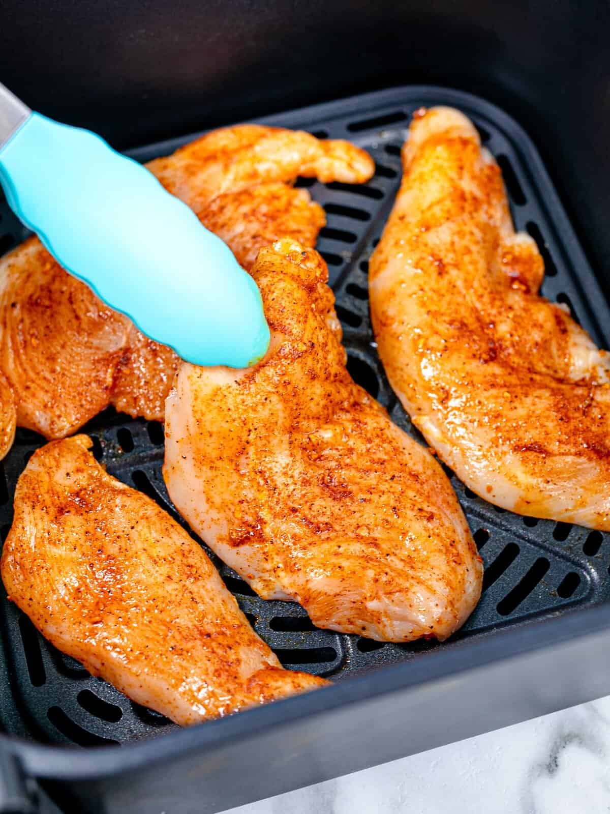 placing seasoned chicken breasts into an air fryer basket. 