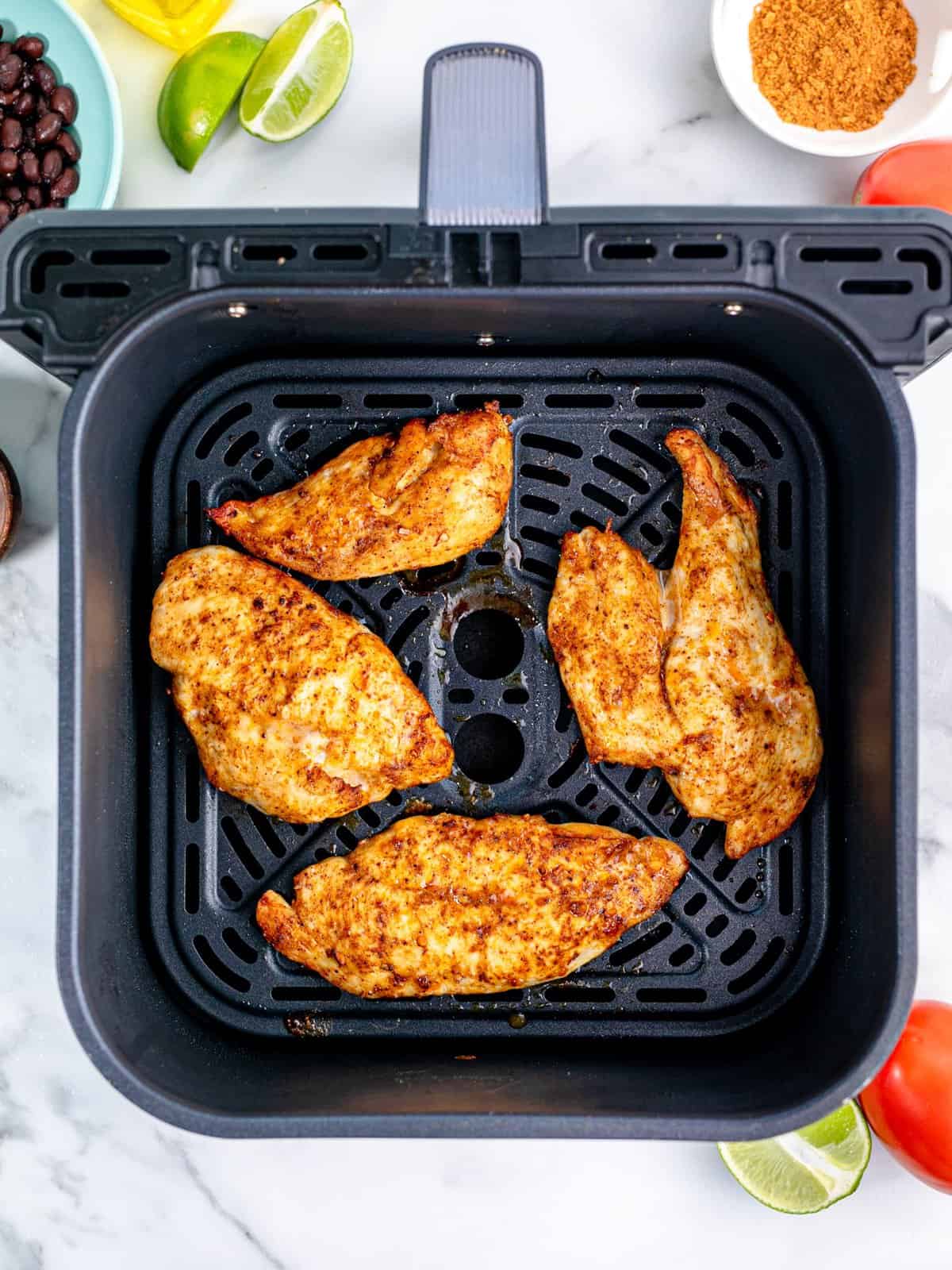 fully cooked chicken breasts shown in an air fryer basket. 
