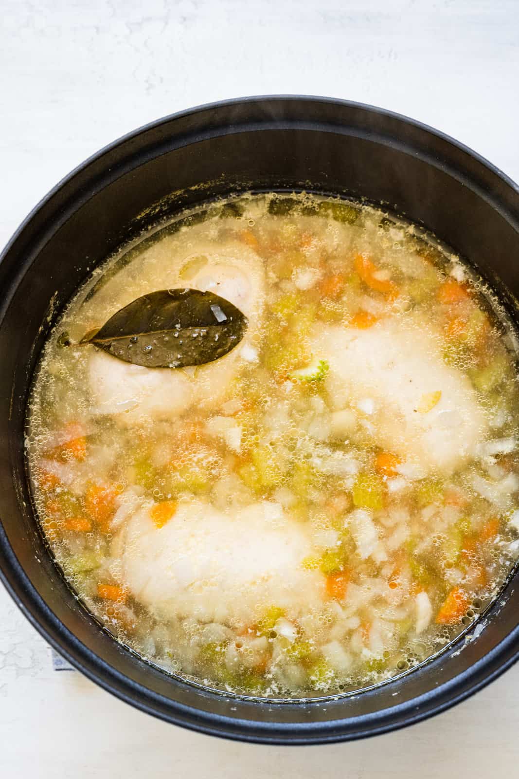 cooked chicken breasts shown in pot with carrots, onions, celery and a bay leaf. 