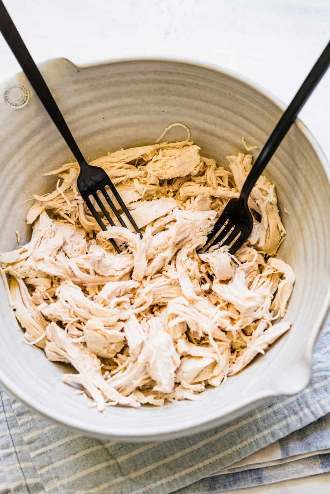cooked chicken being shredded with two forks in a bowl. 
