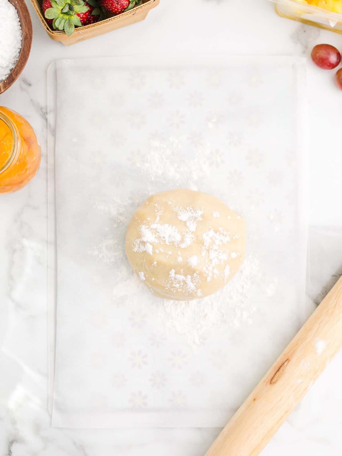 Cookie dough formed into a ball with flour on parchment paper.