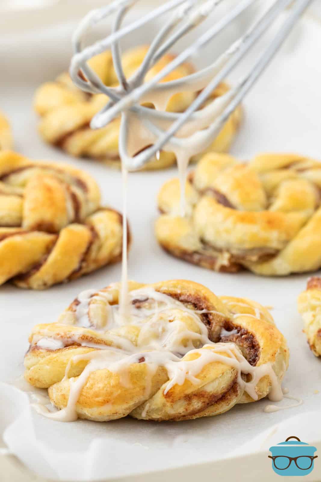 a whisk shown drizzling a powdered sugar icing over the cinnamon knots. 