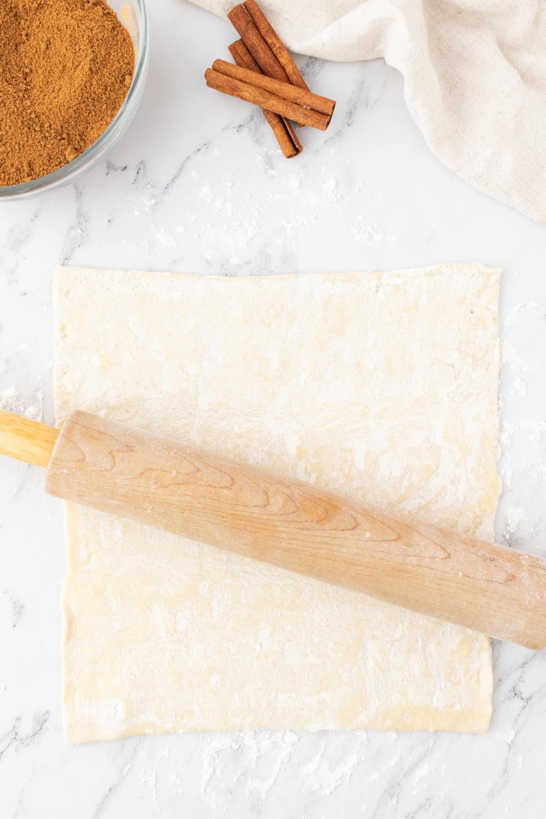 rolling out a sheet of puff pastry with a rolling pin.