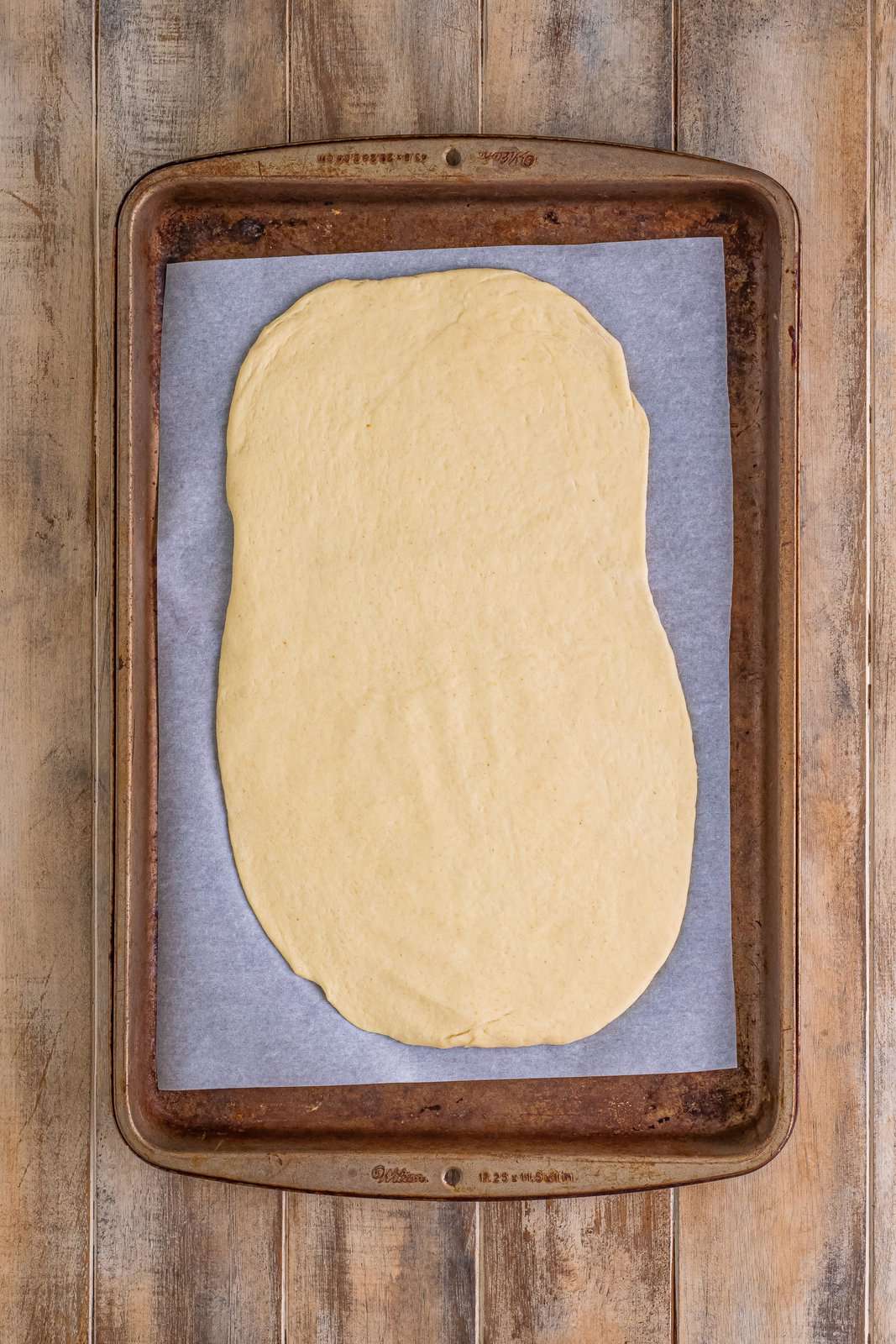 pizza dough spread out on a parchment paper lined baking sheet. 