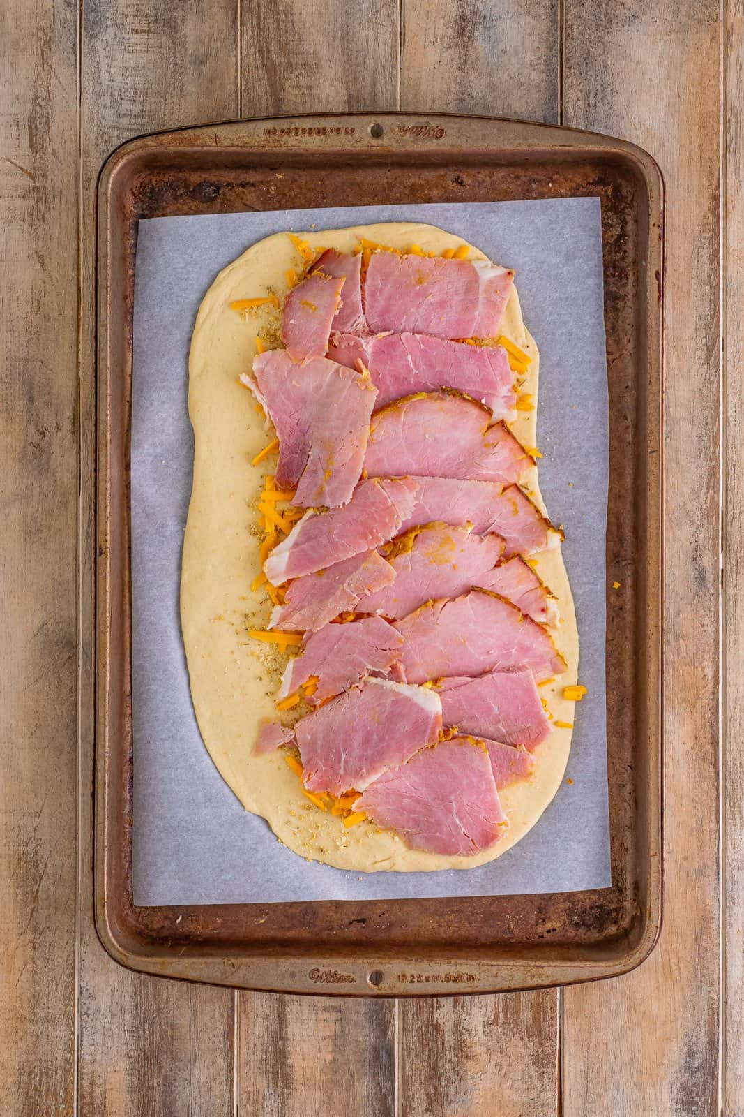 sliced ham layered evenly over cheddar cheese on pizza dough.