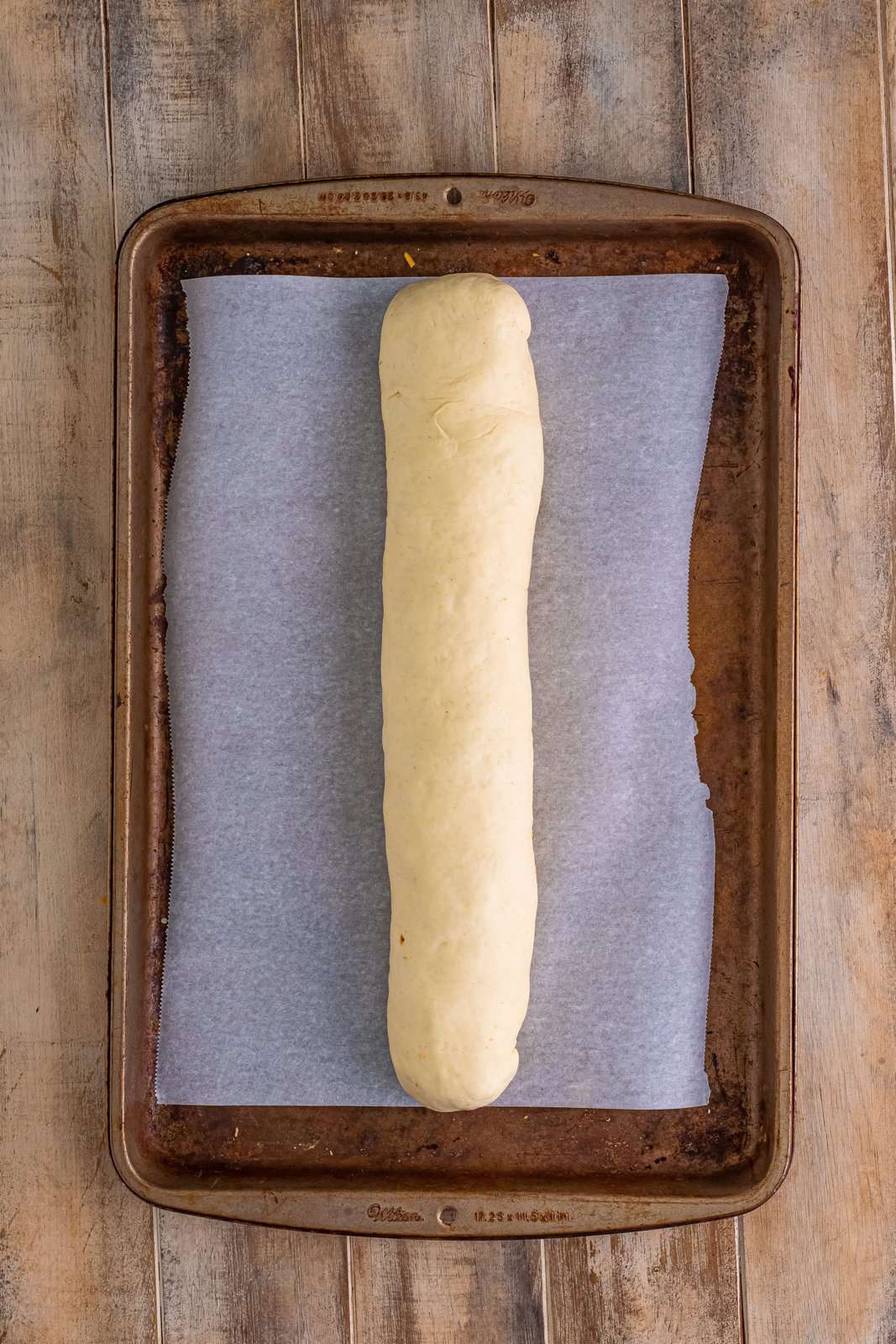 rolled up stuffed pizza dough on parchment paper lined baking sheet. 