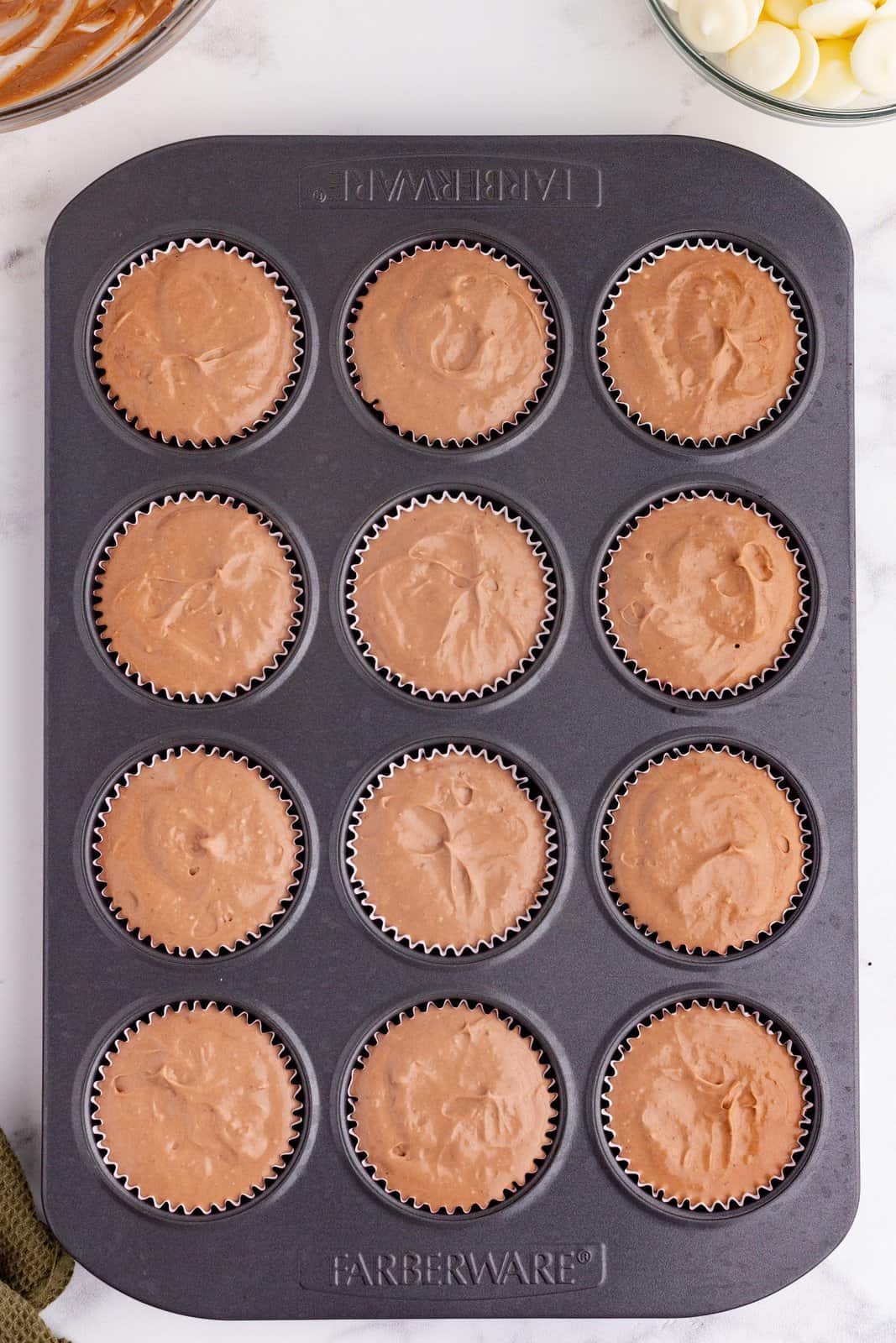 chocolate cheesecake batter added to cupcakes liners in baking pan. 