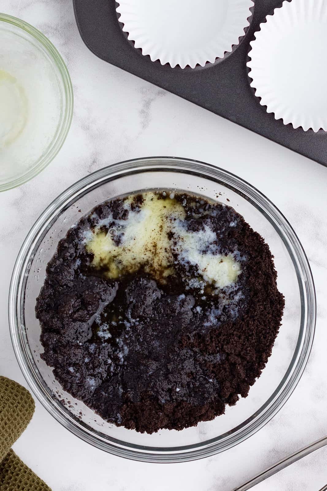 Oreo cookie crumbs combined with melted butter in a bowl.