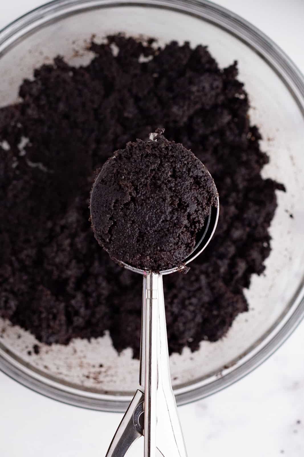 a cookie scoop scooping up some Oreo cookie crumb crust mixture out of a bowl.